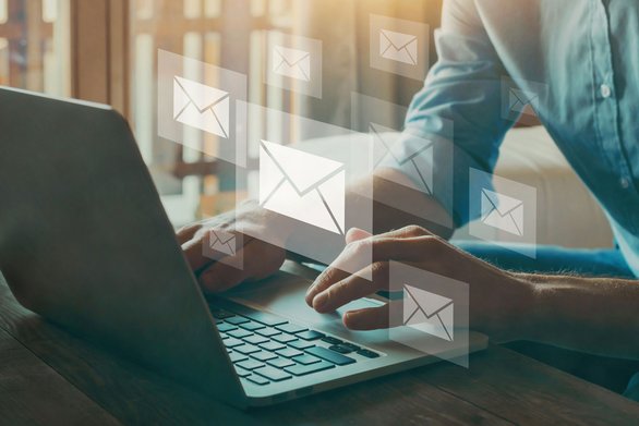 Person am Laptop mit schwebenden Briefsymbolen als Hinweis auf E-Mail-Newsletter.